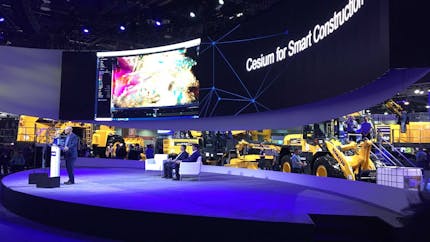 Cesium CEO Patrick Cozzi stands at a podium in front of a wide screen that says "Cesium for Smart Construction" at ConExpo 2020 in Las Vegas
